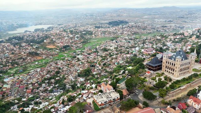 Aerial drone view of Antananarivo cityscape with the Rova of Antananarivo on the hilltop, surrounded by residential neighborhoods and green rice fields in the distance