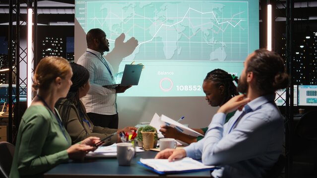 Team of firm coworkers analyzing their pitch ideas for an important meeting, working on ways to obtain more funds. Professional people address financial status at night time. Camera A.
