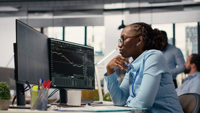 Forex expert in office looking over candlestick charts on screen to assess stock market volatility. African american woman in hedge fund company reading investment reports