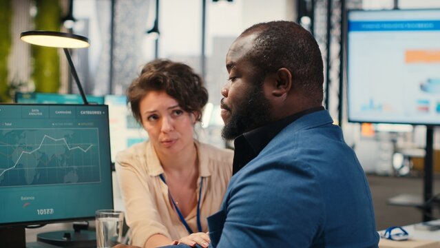 Exasperated black manager dealing with a stressful situation at the office, worried stressed woman colleague trying to calm him down and showing empathy. Trying to avoid a bigger crisis. Camera B.