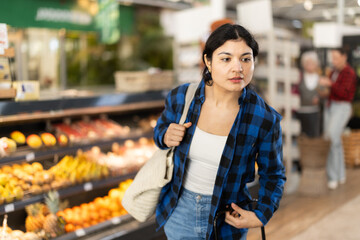 Fototapeta premium Girl in supermarket sales area looks into distance and searches for necessary goods