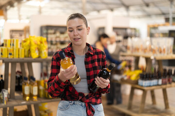 Naklejka premium Girl chooses semi-sweet wine while standing near the shelves with alcohol in a hypermarket. European chooses bottles of wine in a store against the background of customers