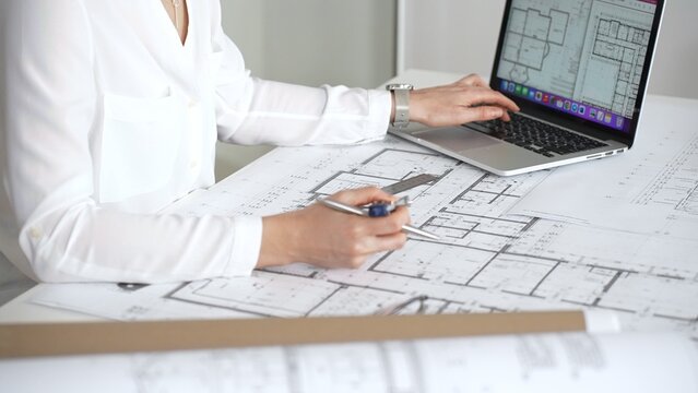 Architect working on building blueprint plans, designing new residential or commercial real estate projects for construction, using a ruler and laptop on a desk