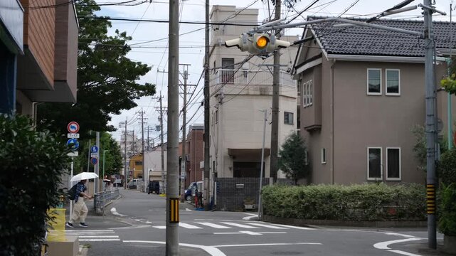 Quiet residential street in Nagoya, Japan with a pedestrian crossing under a flashing traffic signal. Japanese urban neighborhood with overhead cables, narrow roads and local housing.