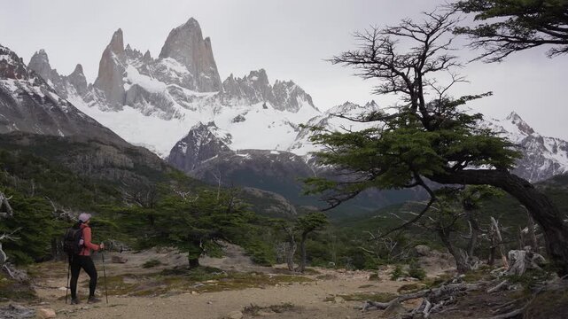 Female hiker walking with the snowy peaks of Mount Fitz Roy behind in nature. Patagonia, Argentina