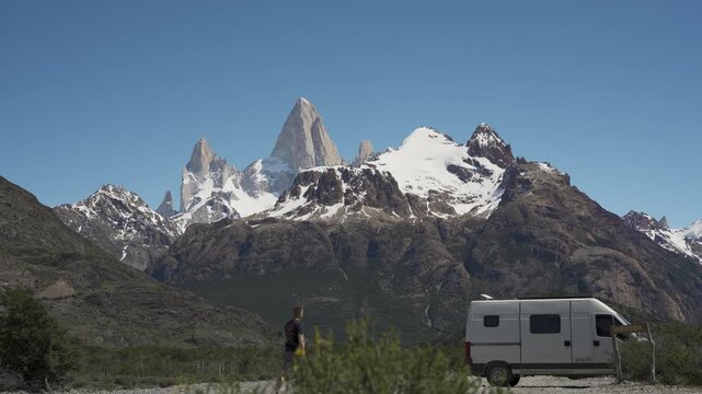 Man standing next to a camper van with a view of Mount Fitz Roy peaks in nature. Patagonia, Argentina