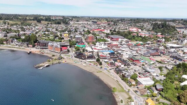 Cinematic aerial shot moving straight forward over the shoreline of Lake Llanquihue, revealing the waterfront hotels and German-inspired architecture of downtown Puerto Varas, Chile