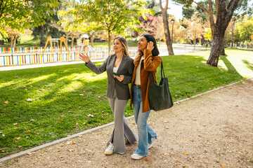 Fototapeta premium Two young women friends enjoying a conversation while strolling through a sunny autumn park