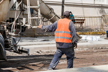 Fototapeta premium Construction worker in orange vest pouring cement on a busy city street