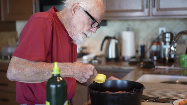 An elderly man prepares his recipe by measuring oil and mixing it into his dish in a home kitchen setting.