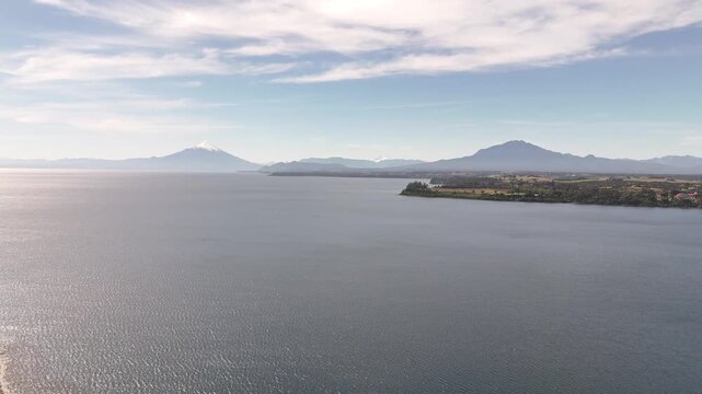 Cinematic aerial moving forward from the Puerto Varas shoreline over Lake Llanquihue, revealing the snow-capped Osorno and Calbuco volcanoes in the Chilean Lake District