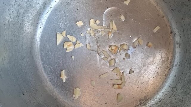 Person putting cooking oil in a pan with chopped garlic