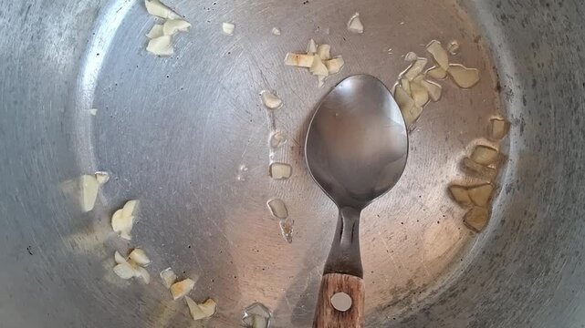 Chopped garlic pieces sizzling in hot oil within a metal pot being stirred video footage