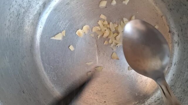 A person removing the remains of chopped garlic from a knife with a spoon