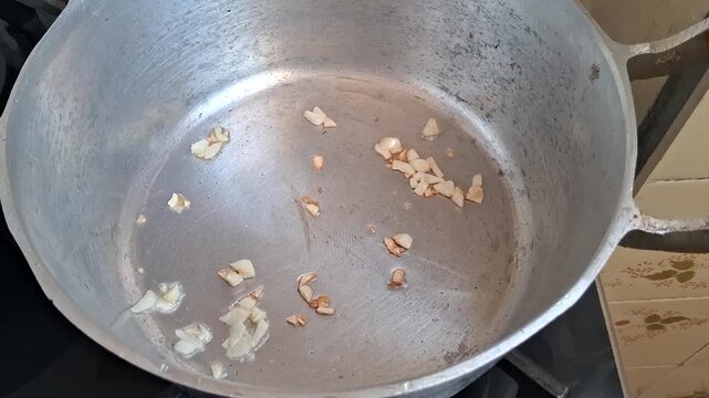 Chopped garlic pieces sizzling and browning in a hot metal pot for cooking footage
