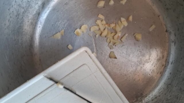 A person pouring chopped garlic into an empty pan