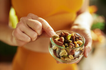 Detail of a person selecting a pistachio from a glass bowl of mixed nuts, focusing on healthy snack...