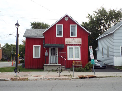 Ottawa, Ontario, Canada-July 22, 2025: The vibrant red exterior of "Konson Homes" features white-trimmed windows, a small porch, and a wooden bench along the sidewalk at 361 Churchill Ave N.
