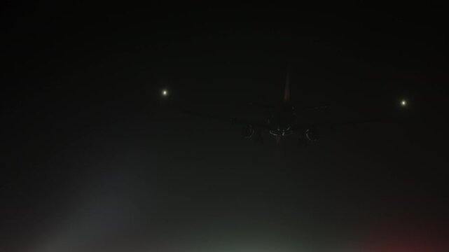 Airplane approaching a brightly lit runway at night, followed by a ground-level view of the dazzling red, green, and white runway lights through haze