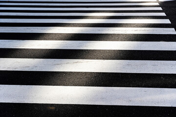 Black and white pedestrian crosswalk stripes on asphalt road with strong contrast and geometric pattern.