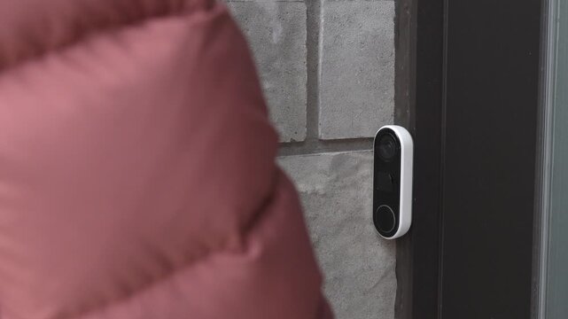 Person in brown puffer jacket approaches a doorbell camera mounted on a stone wall, preparing to interact with the device at the entrance