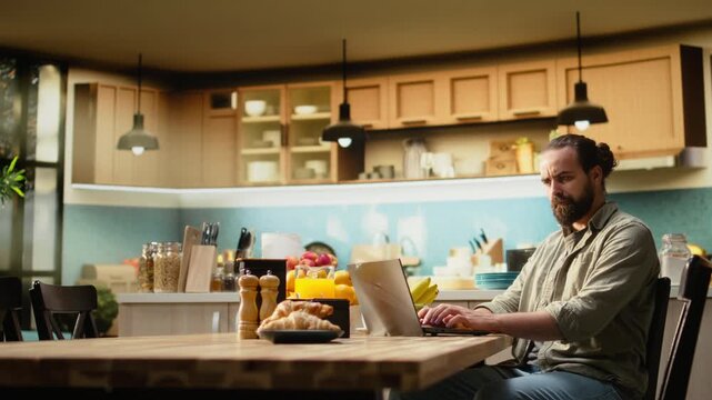 Uncertain freelancer being confused about ambiguous tasks at home, remote work on laptop in the kitchen. Disoriented disorganized man unsure about telecommuting job, frowning.