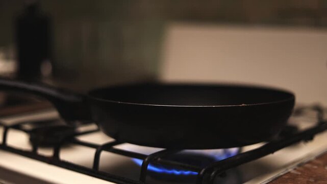 Frying pan heating up on a gas stove with blue flames visible