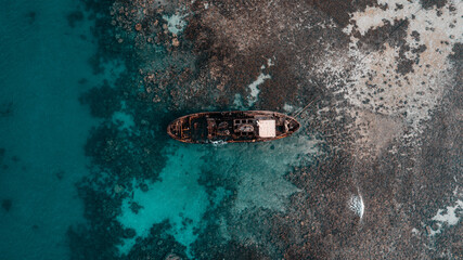 Aerial view of an abandoned shipwreck in the turquoise waters of the Red Sea near the Ship Graveyard in Al-Shuaiba, south of Jeddah, Saudi Arabia. The rusted vessel rests among coral reefs and shallow © Mohammed