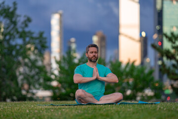 Fototapeta premium Man meditating with peaceful expression. Man practicing yoga outdoors in nature. Man sitting in lotus meditation pose. Man enjoying calm wellness moment.
