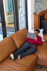 Naklejka premium African American child reclining on right of tan leather couch holding tablet wearing white headset