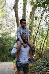 Naklejka premium African American father and child walking on paved trail, child riding on shoulders, zip-up hoodies