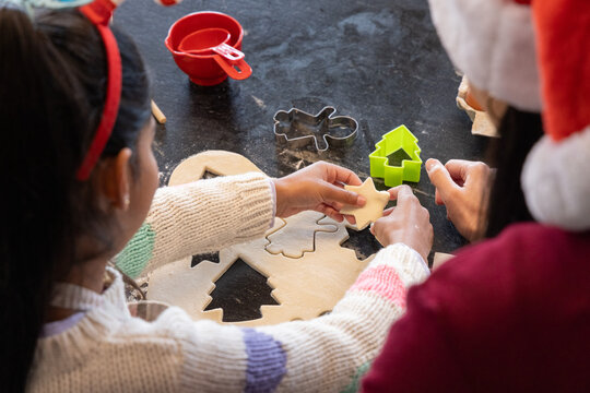 Parent and child cutting cookies on dark kitchen countertop, holding star dough, wearing Santa hat