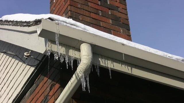 Frozen eavestrough with downspout and icicles. HD video. 