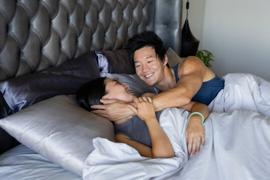 Smiling couple lying on bed in bedroom, man cradling woman's head, navy tank, gray top visible