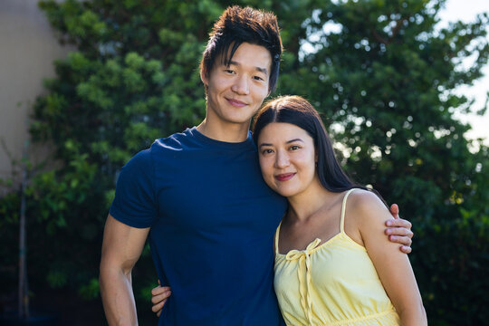 Diverse couple leaning in sunny garden, man in navy tee, woman in pale-yellow dress with tie