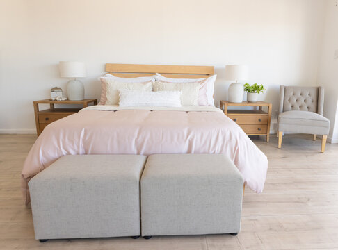 Natural light entering from right illuminating wooden bed in bedroom with blush duvet and pillows