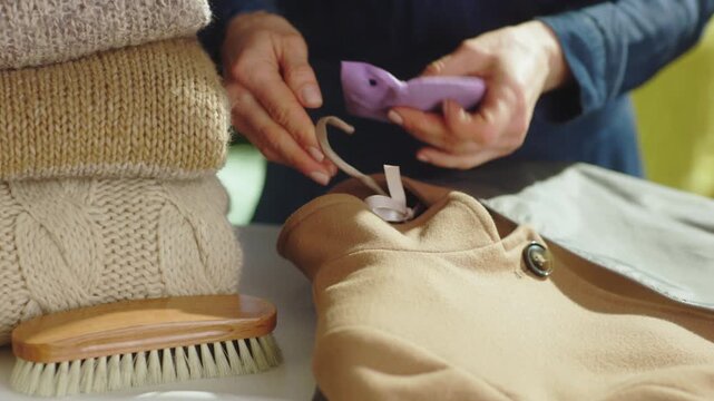 A woman places a purple sachet on a coat hanger, ensuring freshness and moth protection before storing winter garments in the closet.