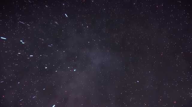 A dark night sky filled with stars and streaks of light, with blurred smoky patches