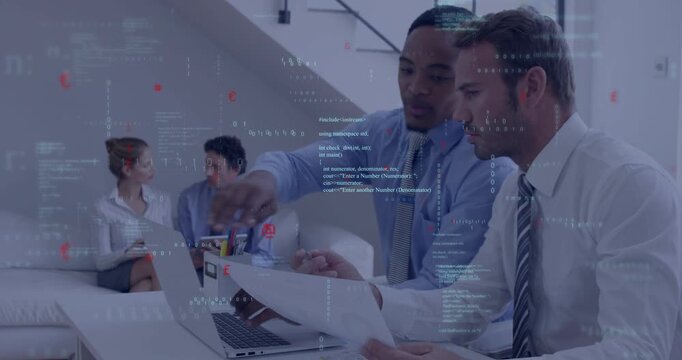 Two men pointing at laptop then typing while reviewing documents in business meeting, smiling