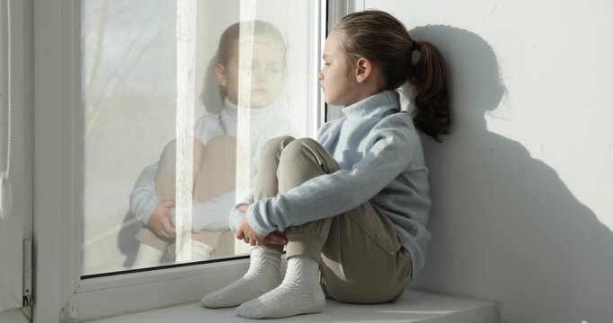 Autism. Little girl on window sill indoors