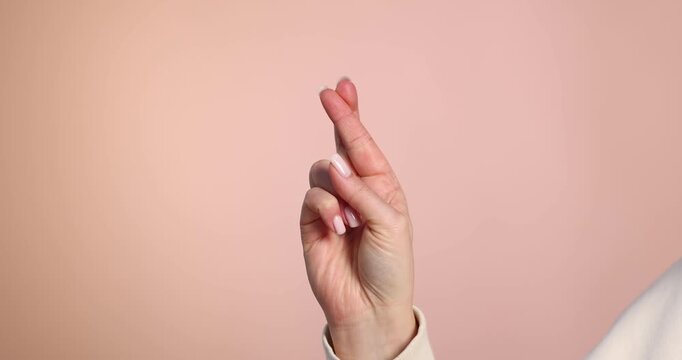 Woman crossing her fingers on beige background, closeup