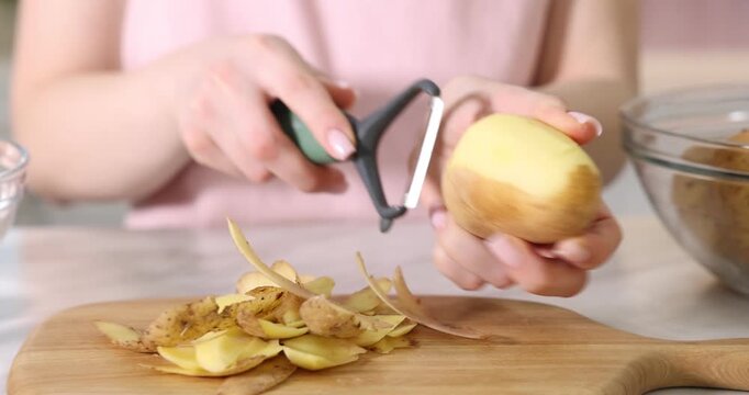 Woman peeling fresh potato at white marble table indoors, closeup. Camera moving forward