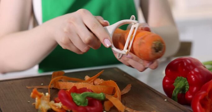 Woman peeling fresh carrot at white table with vegetables indoors, closeup. Camera moving forward