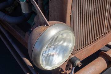 Fototapeta premium Close-up of heavily weathered rust-colored round fluted glass lens headlight assembly and vertical radiator grill of a vintage car