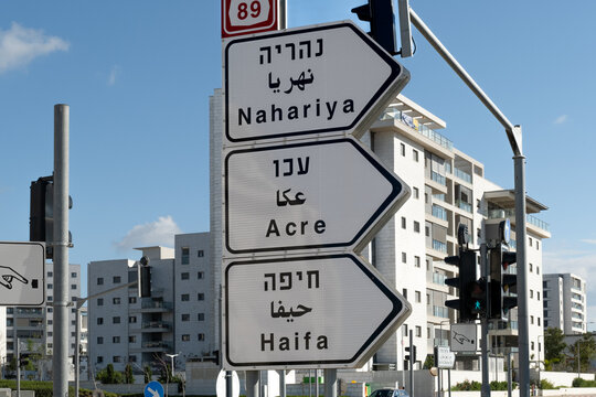 Directional road signs in Israel  white pointer sign displays distances to Nahariya Acre and Haifa in three languages. This street scene represents the concept of multilingual traffic navigation