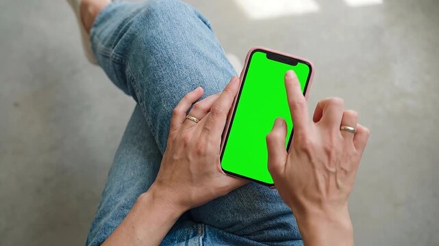Close-up of a person's hands holding a modern mobile phone with a bright green screen, demonstrating user interaction with the device for various applications