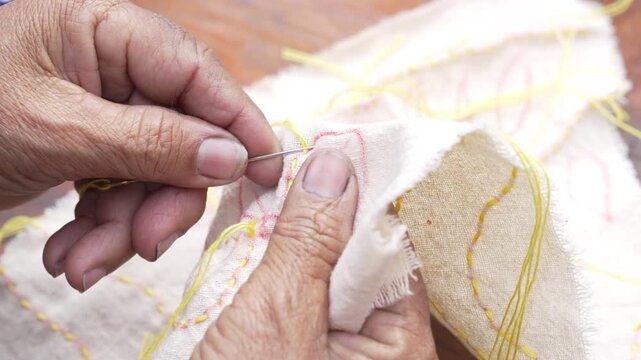 Elderly Hands Skillfully Embroidering White Fabric with Yellow Thread, Showcasing Traditional Craftsmanship and Attention to Detail