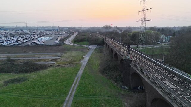 Drone follows the railway bridge with drifting smoke trees logport and moving trucks visible to the side.