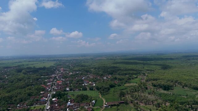 Cinematic aerial view of a rural village and teak forest with Mount Lawu on the distant horizon, Ngawi.