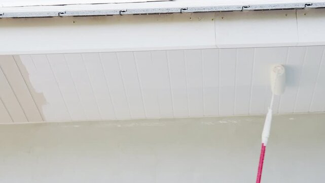 Close up of paint roller applying white paint on ceiling during home renovation. Interior improvement, house maintenance and professional construction work concept in residential building.